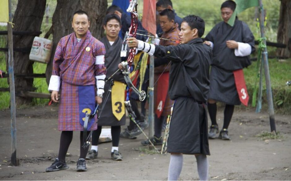 Customs and Traditions in Bhutan - Image of local Bhutanese men holding bows and arrows with a man in a black robe at the front pointing his arrow off to the side of the image.