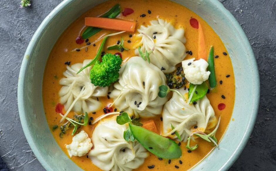 Customs and traditions in Bhutan - A closeup of Momos dish with dumplings sat on a bed of thick orange-cololured sauce